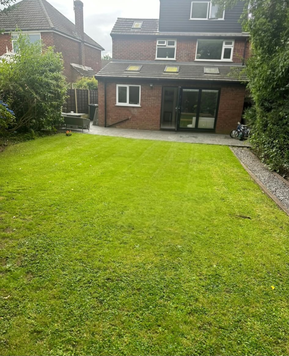 Finished Romiley rear extension and dormer loft seen from the garden, with a paved patio, lawn and glazed doors
